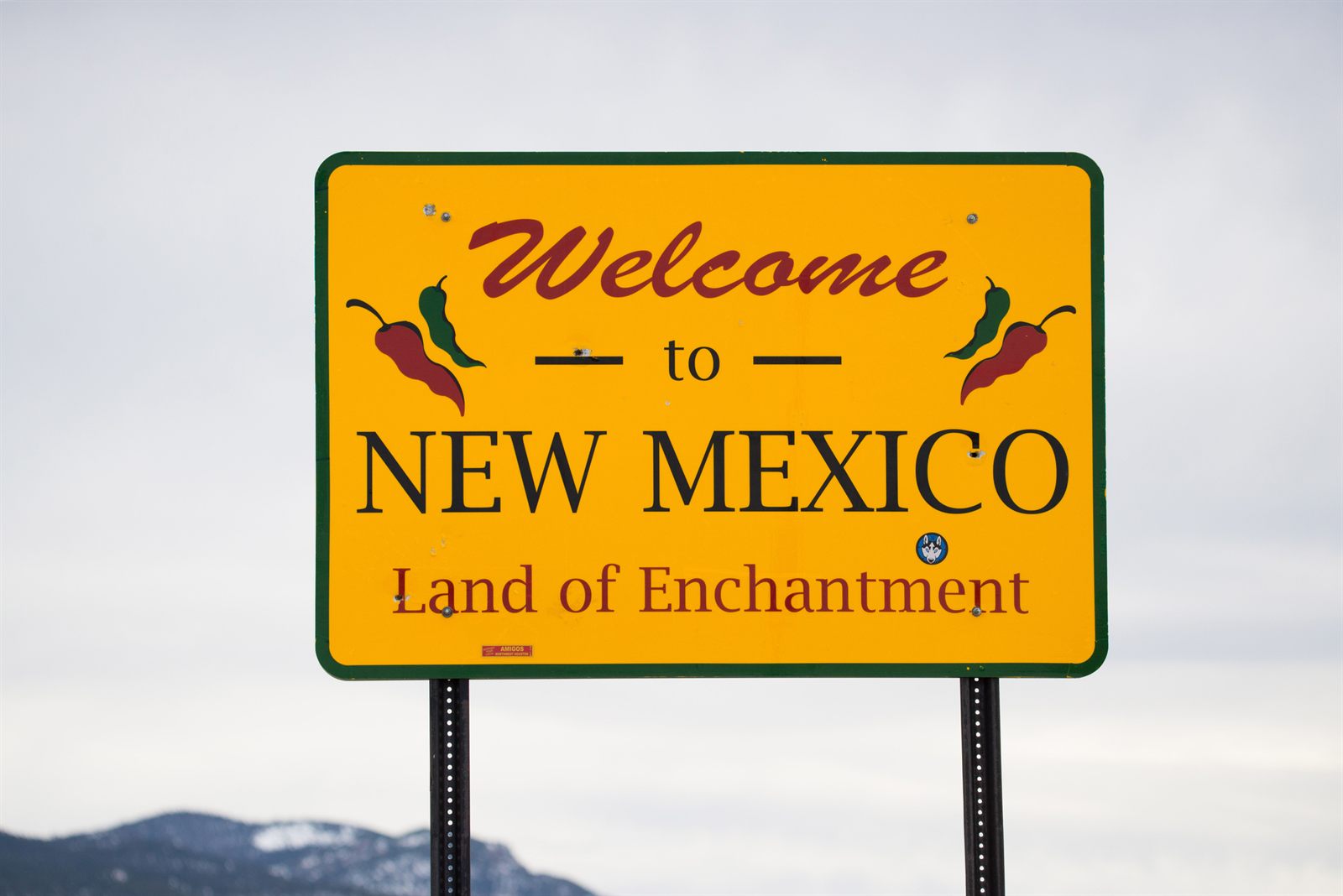 A yellow Welcome to New Mexico, Land of Enchantment road sign decorated with red chiles